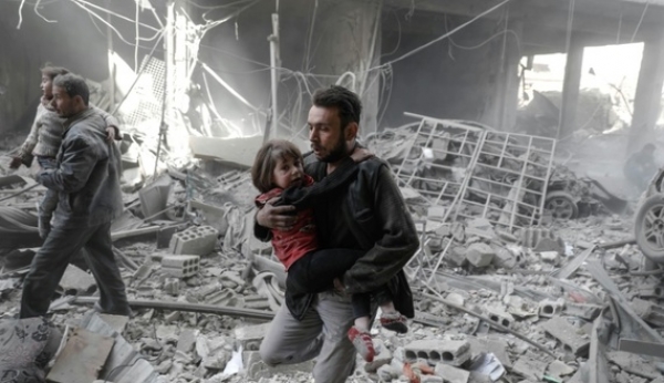 Uomini portano in salvo dei bambini da edifici distrutti dai bombardamenti